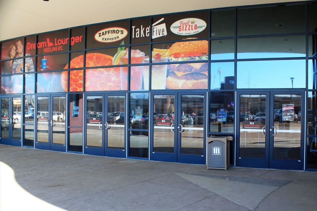 Storefront with glass doors, blue trim, and large food-themed window signage in a shopping center