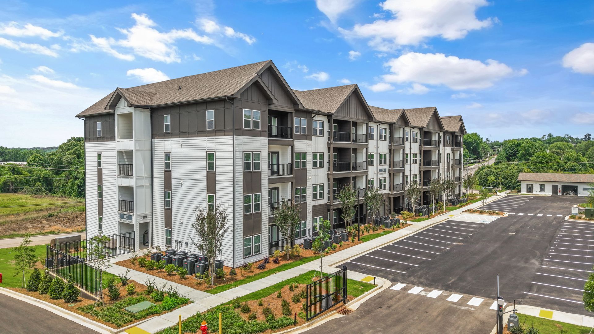 Modern apartment complex with gray siding, balconies, and a large parking lot on a sunny day