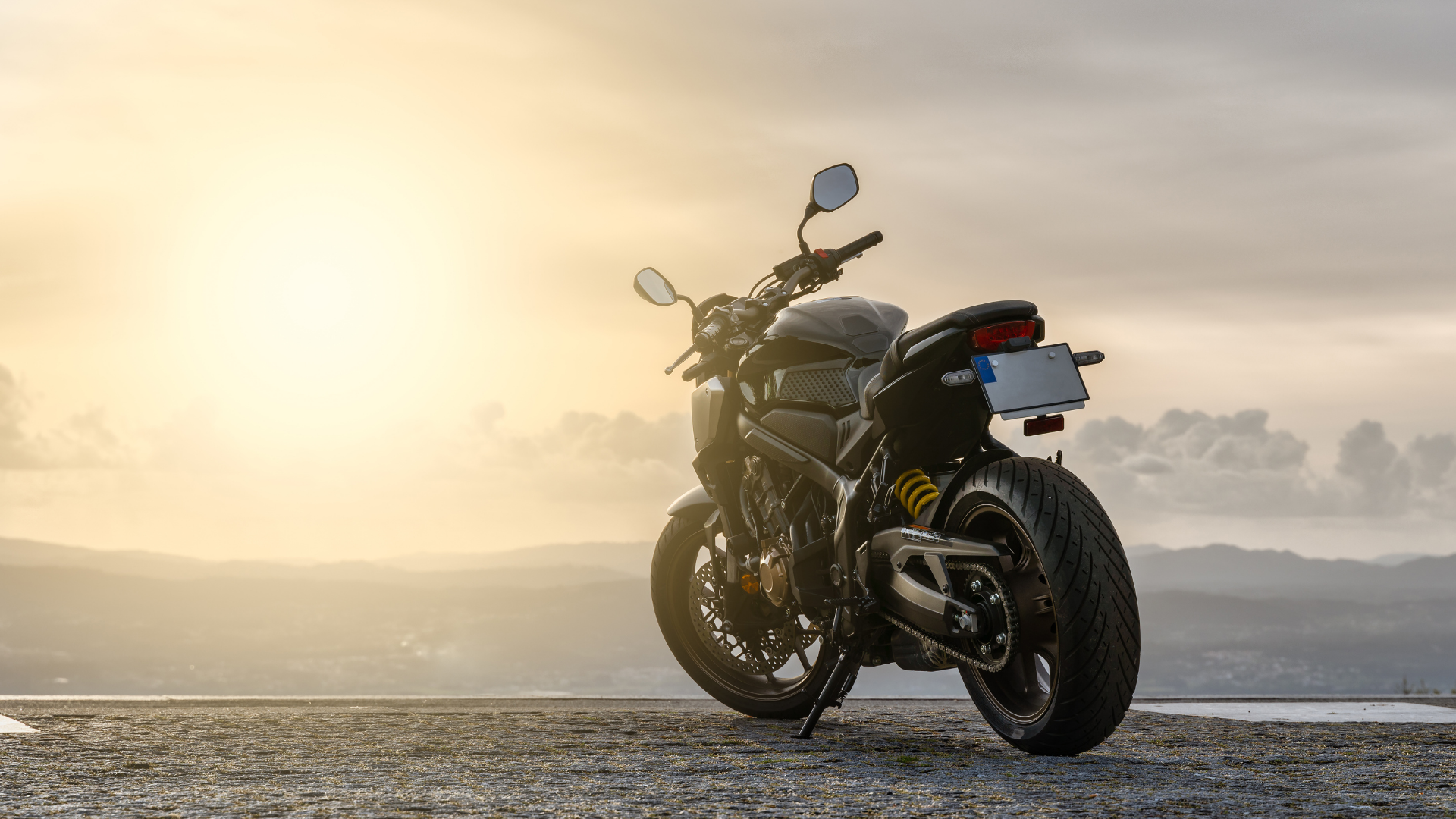 Motorcycle parked on a road at sunrise, silhouetted against a misty golden sky.