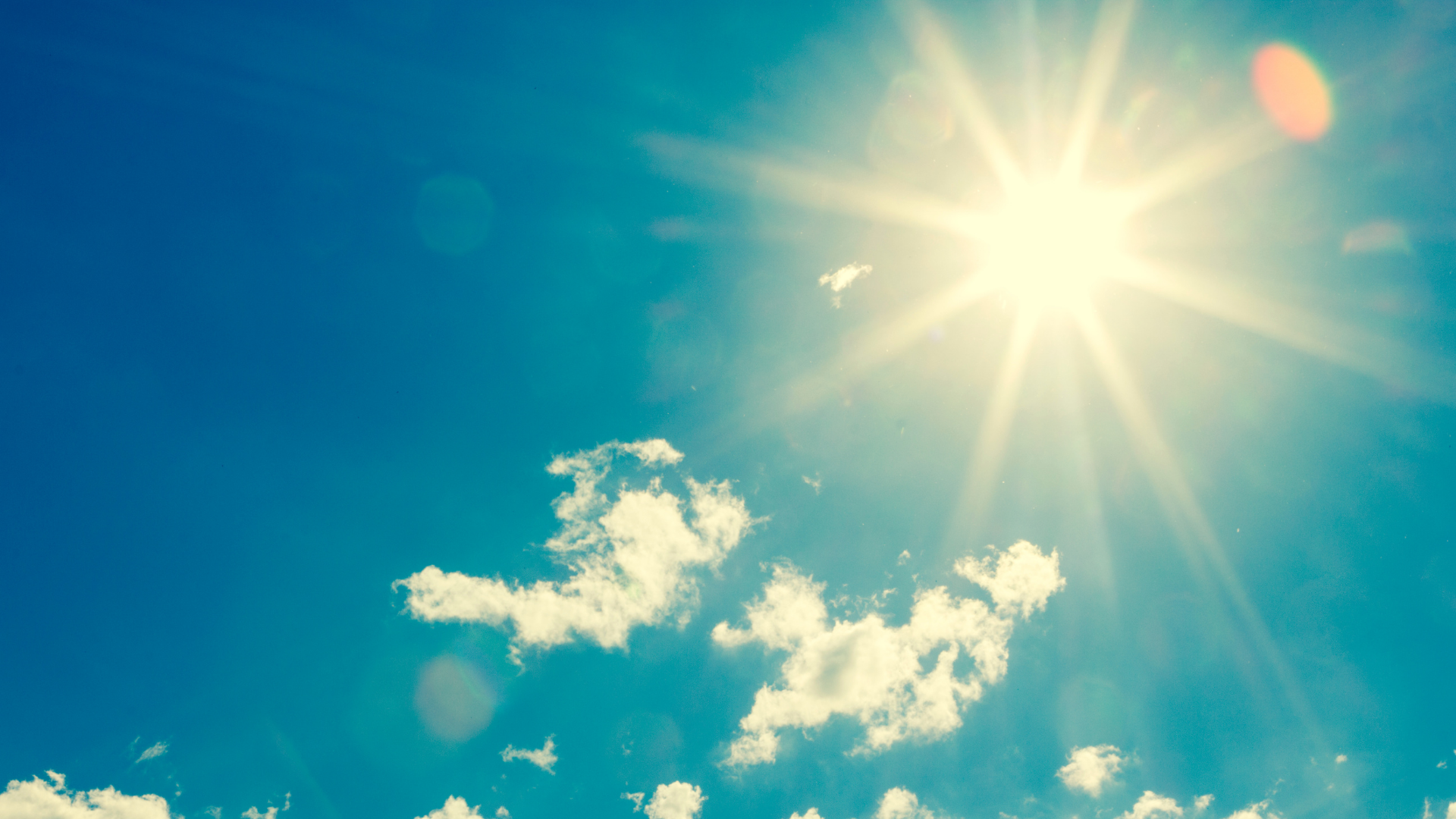 Bright blue sky with sun glare and scattered white clouds