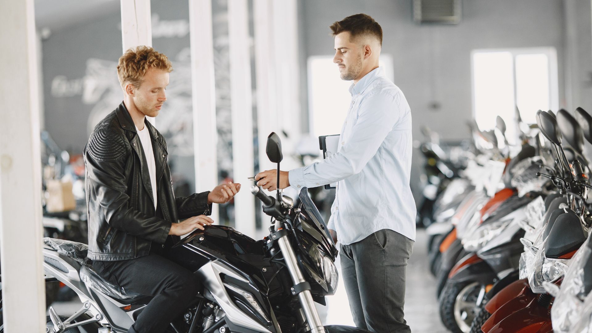 Two men discussing a black motorcycle in a bright showroom with rows of bikes.