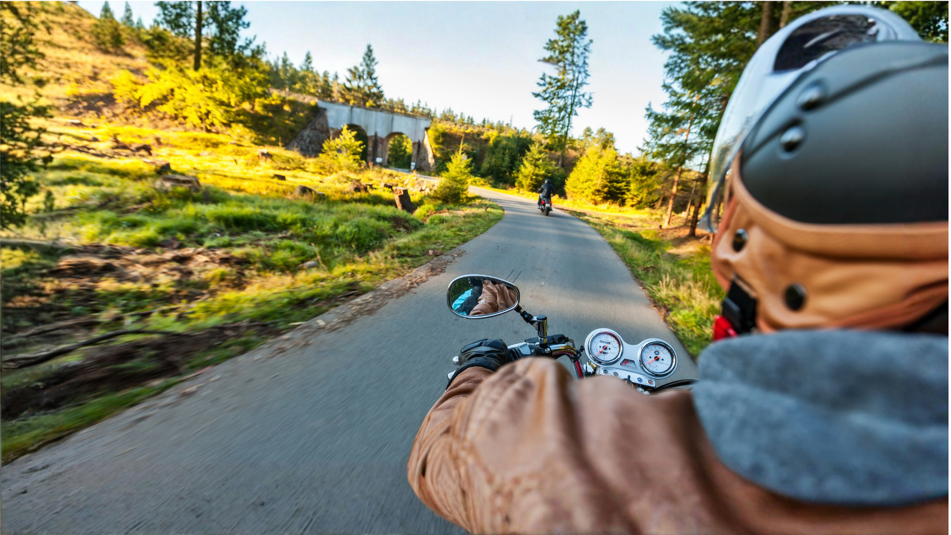 Cyclist riding downhill on a sunlit paved trail through a forested hillside