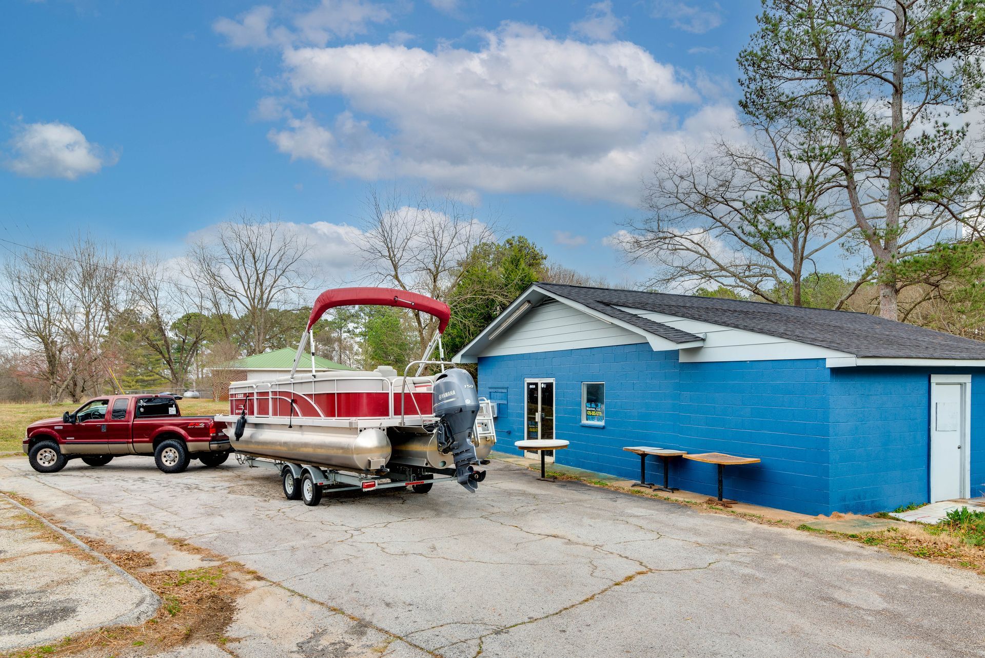 A pontoon boat is being towed by a truck in front of a blue building.