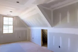 Unfinished room with drywall on walls and angled ceiling. Window on left, doorway on right.