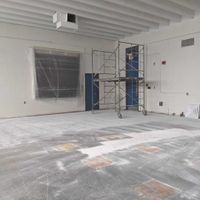 Interior of room under construction; scaffolding, covered window, unfinished floor.