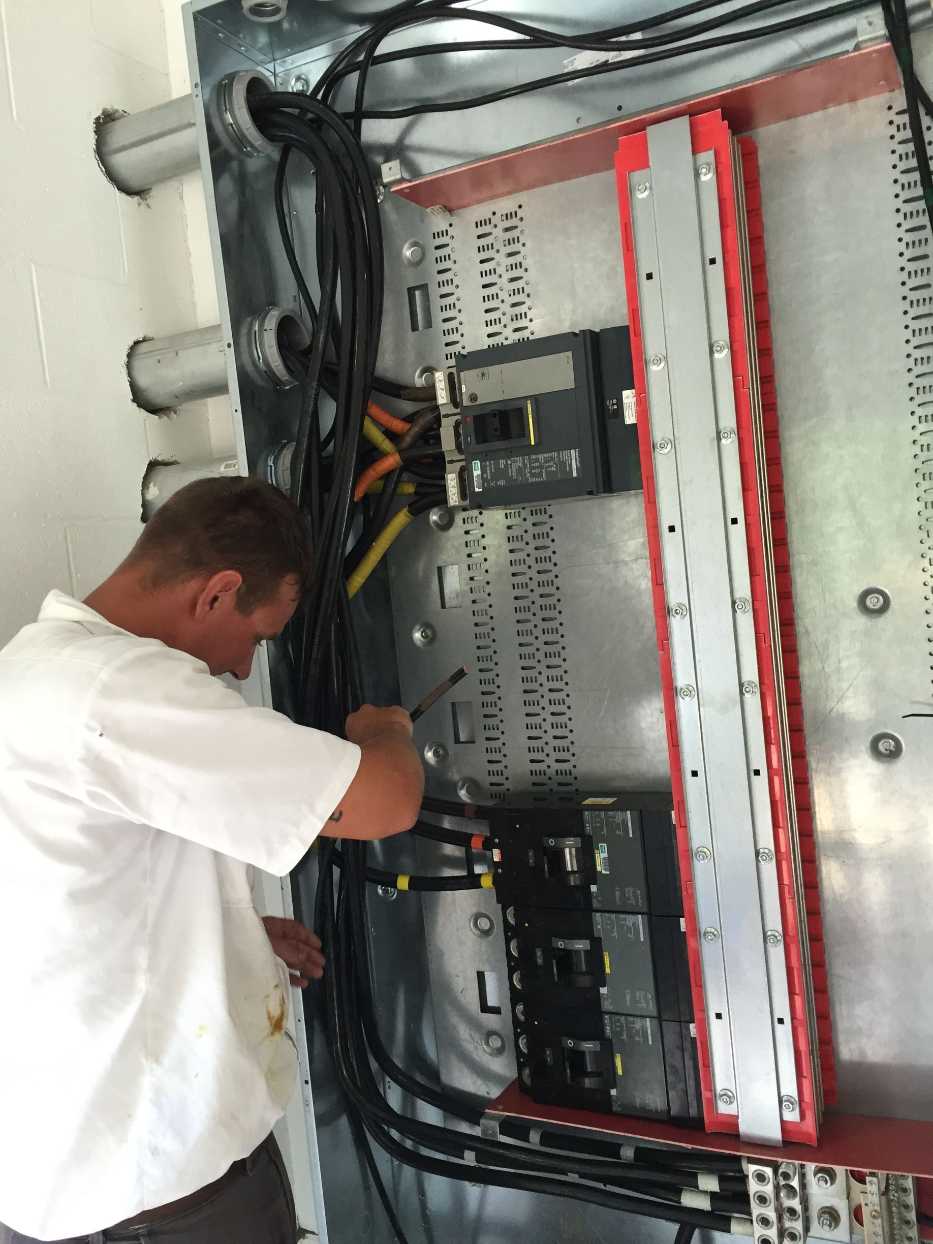 Electrician working on electrical panel, using a tool. Panel is silver with red trim, and black wires.