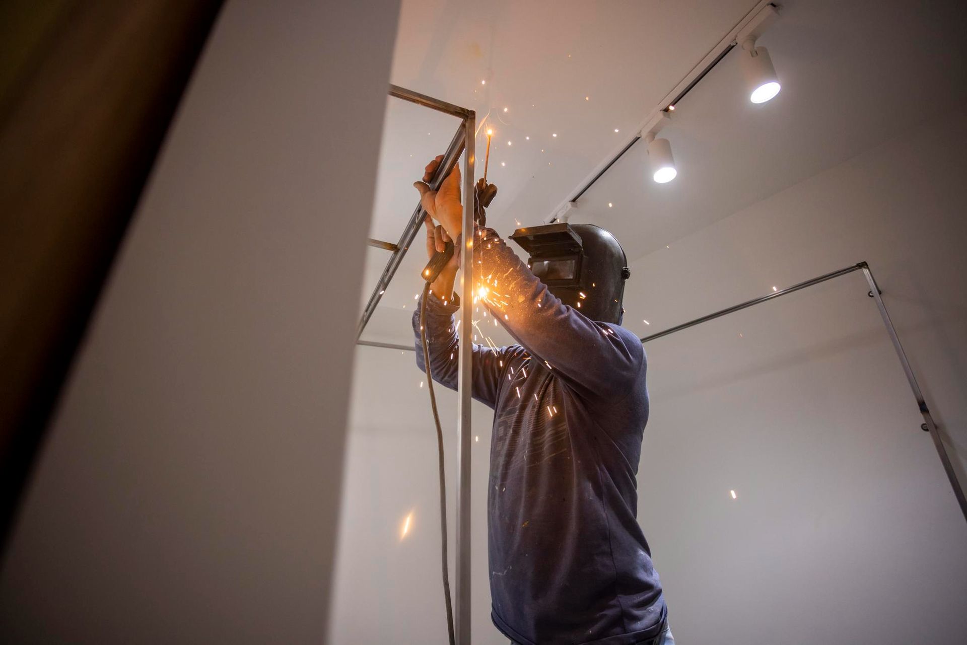 Person welding metal frame in a bright room, sparks flying.