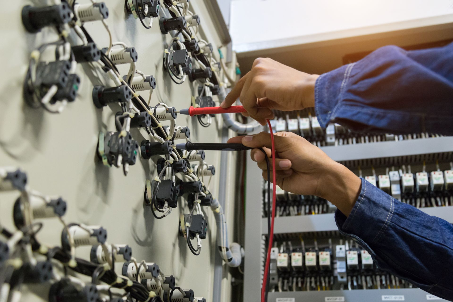 Person using multimeter probes to test electrical wiring in a control panel.