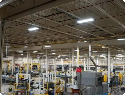 Factory interior with machinery, overhead crane, and workers.