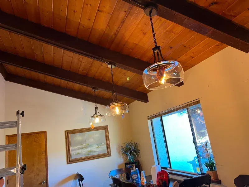 Wooden ceiling with pendant lights above a dining table near a window.