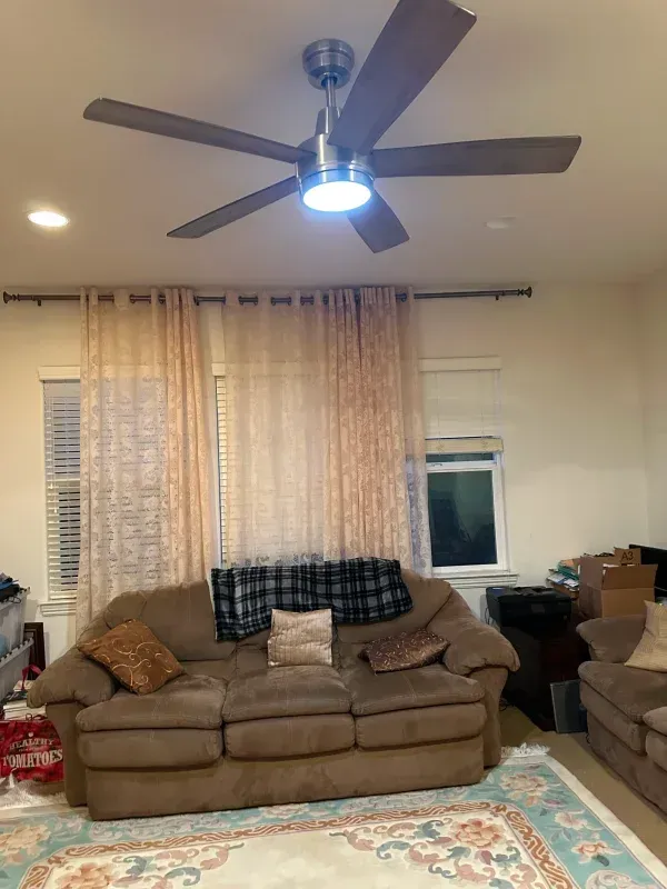 Living room with brown sofa, ceiling fan, sheer curtains, and area rug.