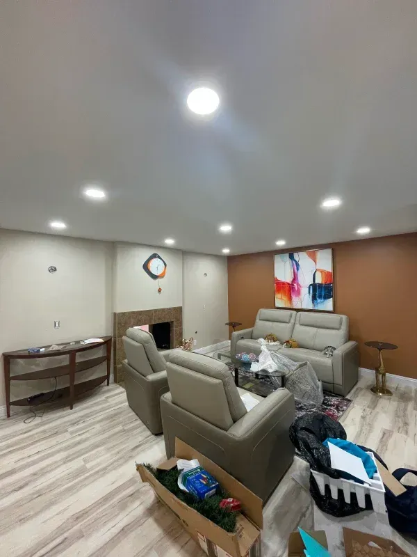 Living room with furniture, overhead lights, fireplace, and abstract art. Tan and orange walls, light-colored flooring.