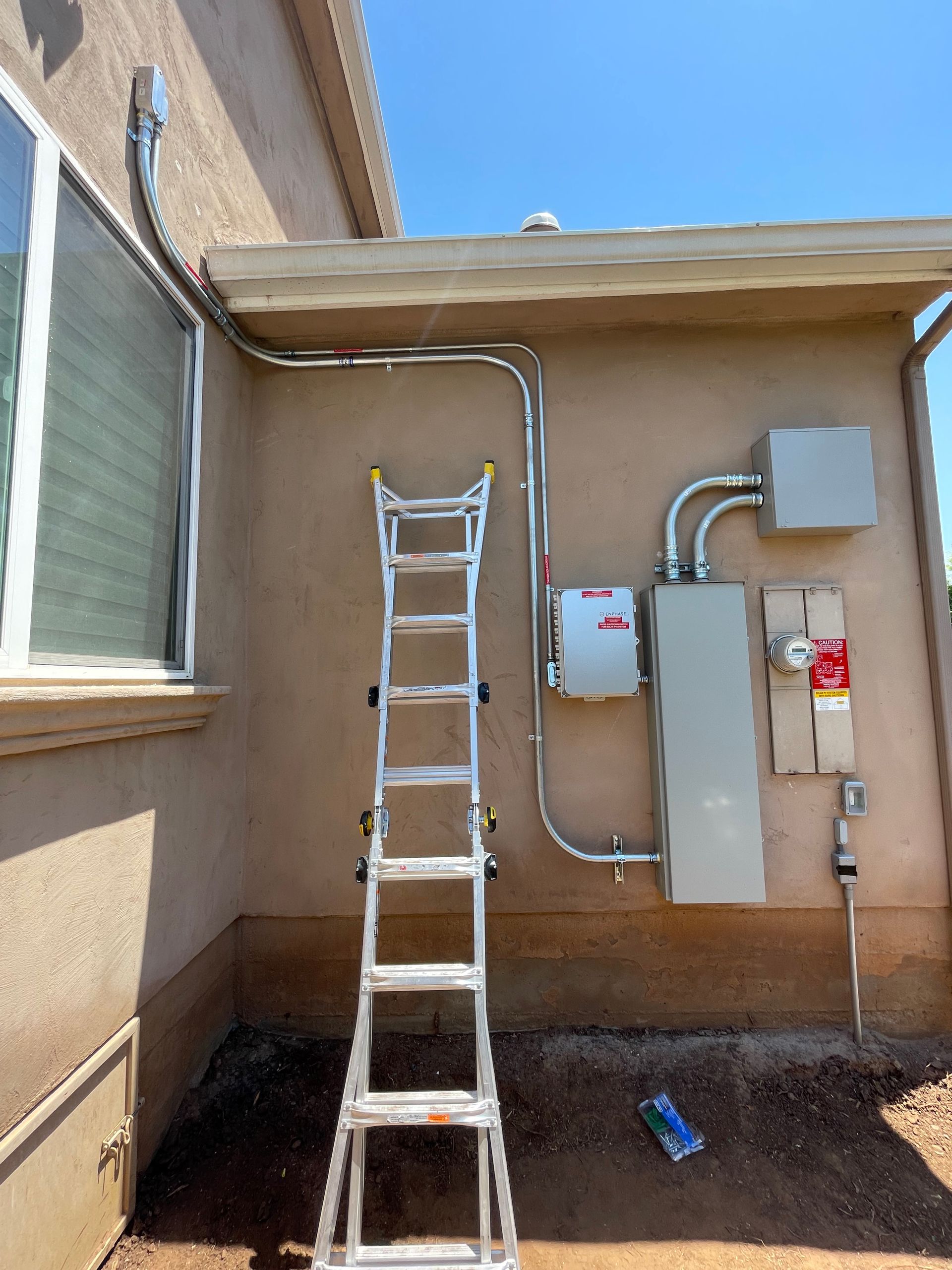 Electrical equipment installed on a beige building exterior with a ladder in front.