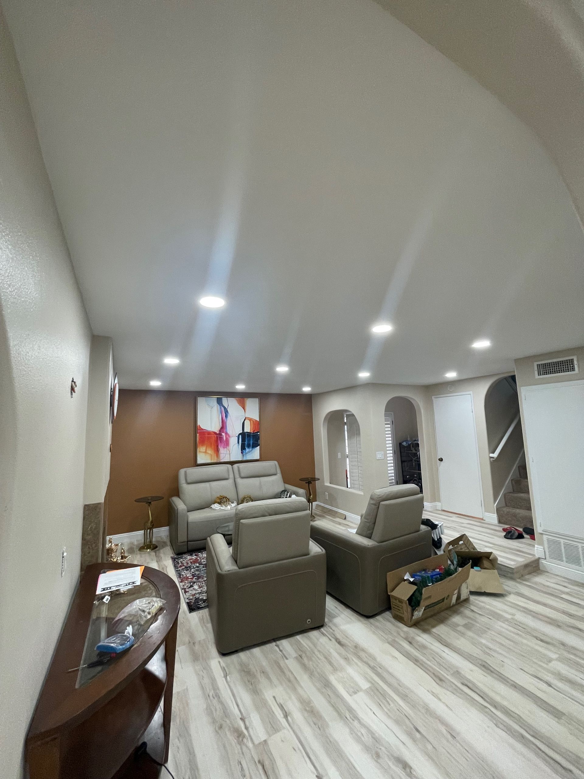 Living room with sofas, armchairs, artwork, and recessed lighting; white walls and wood floor.