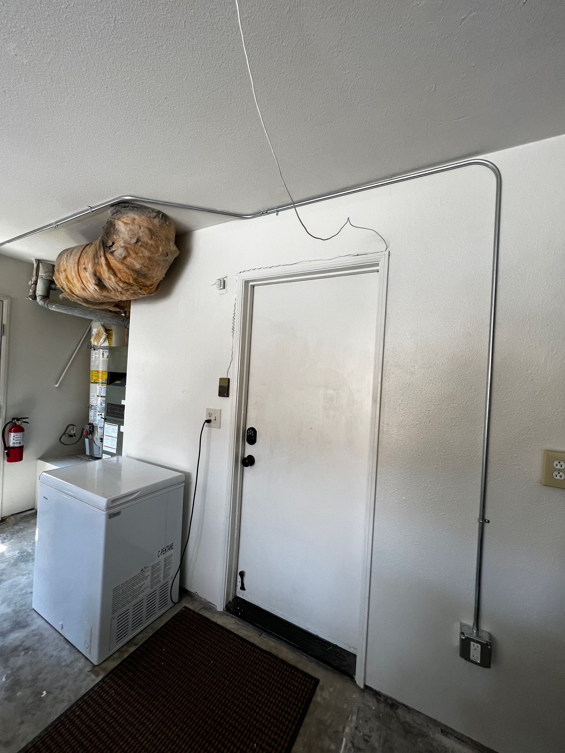 White door in a room with a freezer, vent, and electrical wiring.