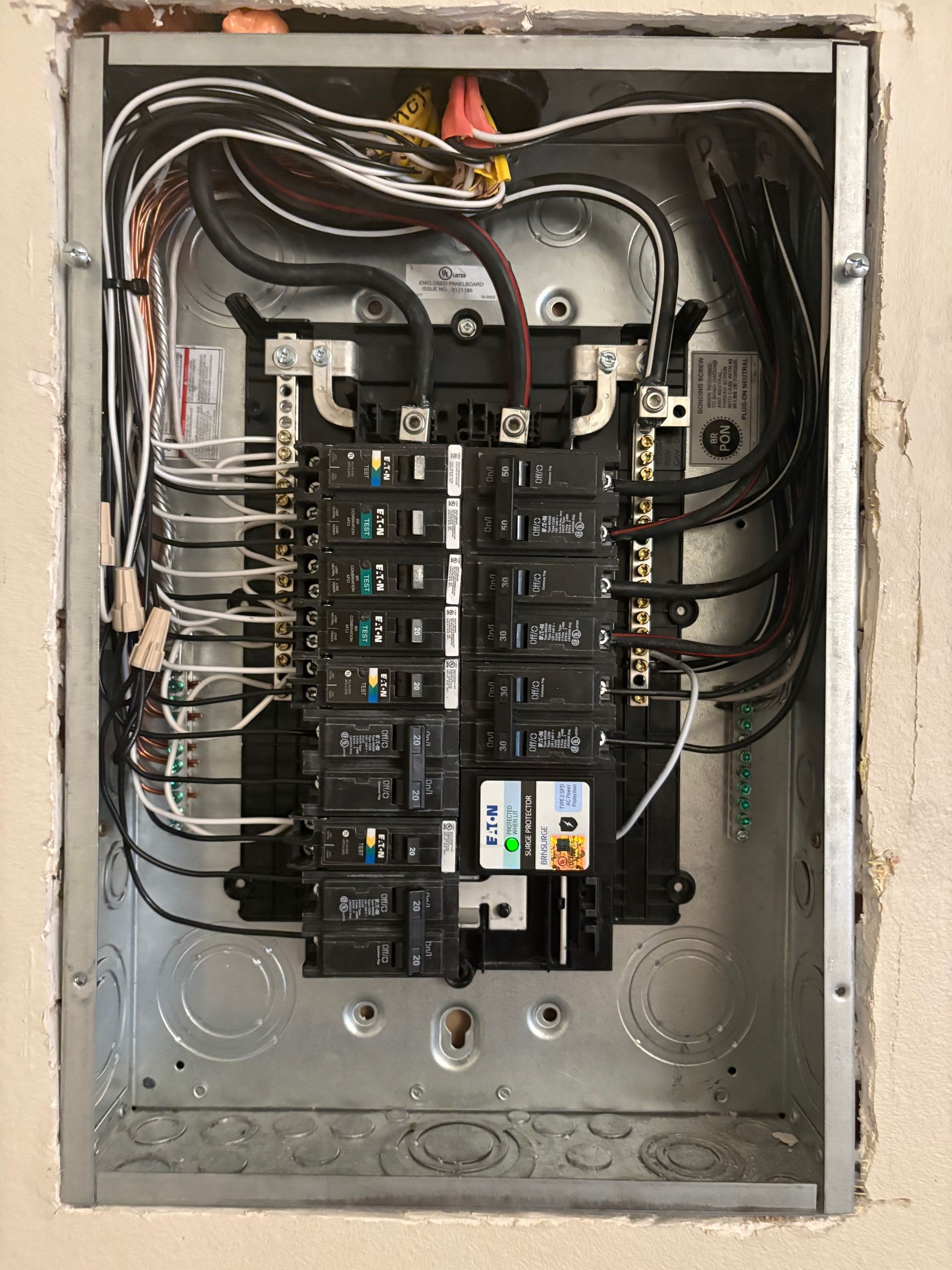 Electrical circuit breaker panel with wires and breakers installed inside a metal box in a wall.