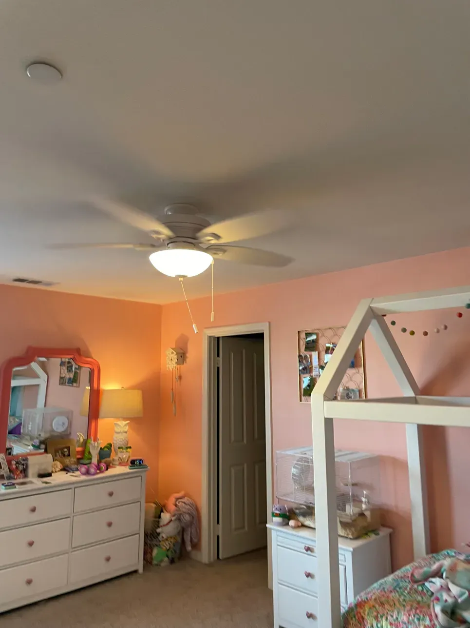 Pink bedroom with dresser, bed frame, ceiling fan, and open door.