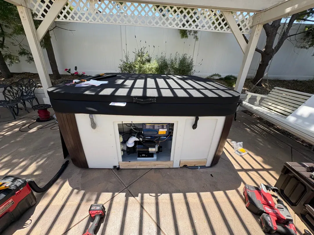 Hot tub with open panel, under a white trellis. Tools are scattered nearby.