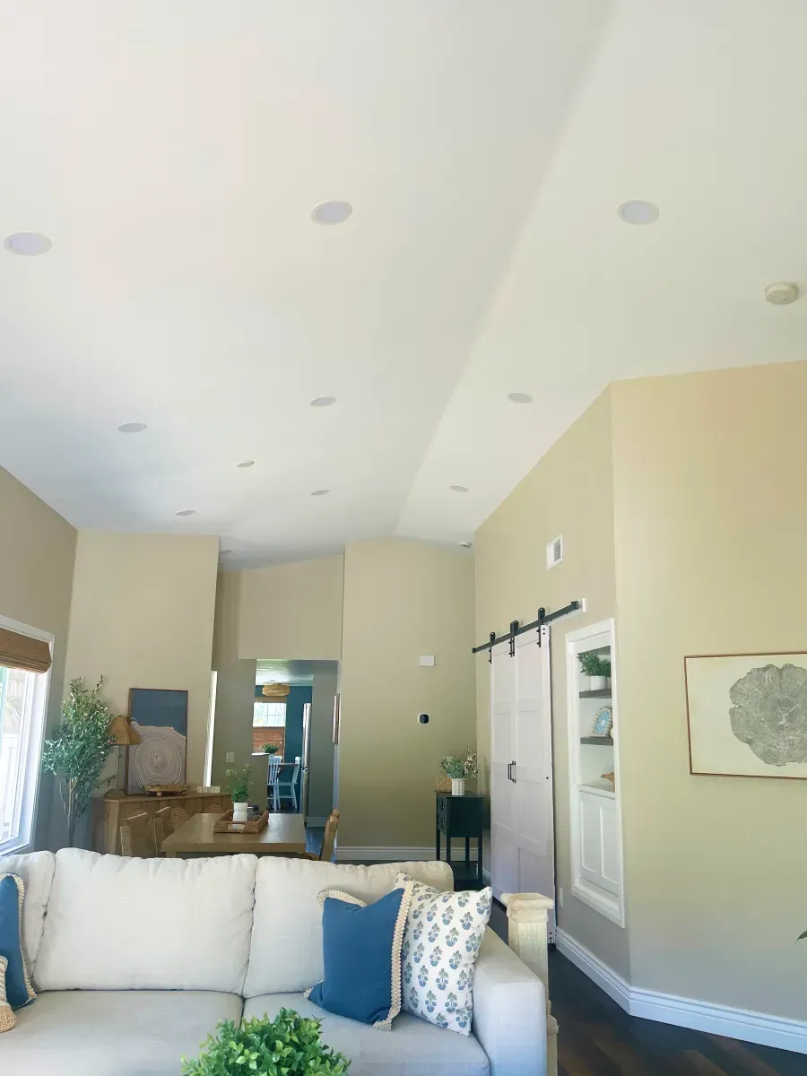 Living room with white ceiling, beige walls, recessed lights, and white couch with blue pillows.