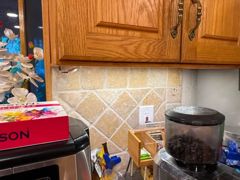 Kitchen counter with backsplash, cabinets, appliances, and a red light switch.