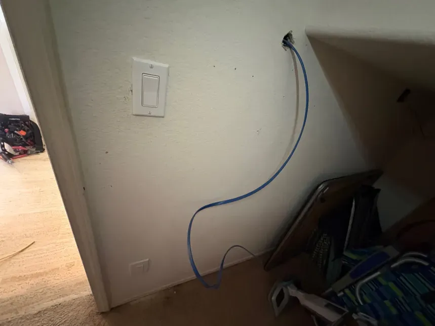 Blue network cable emerging from wall, near light switch. Chair and clutter in corner.