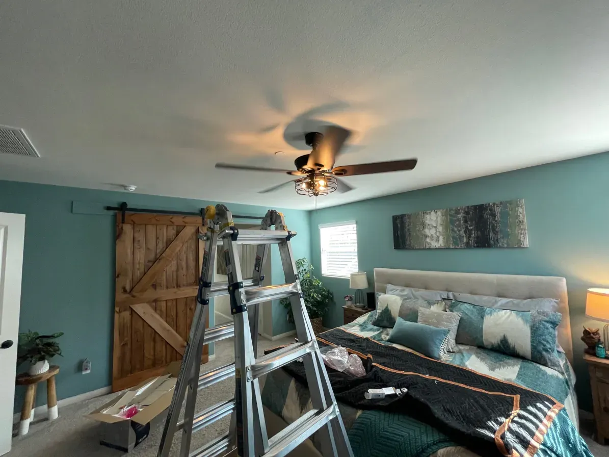 Bedroom with teal walls, barn door, and a ceiling fan; ladder in front of bed.