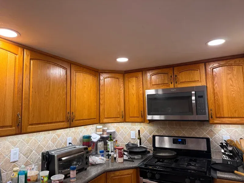 Oak kitchen cabinets and a microwave above a stove with a patterned backsplash and recessed lighting.