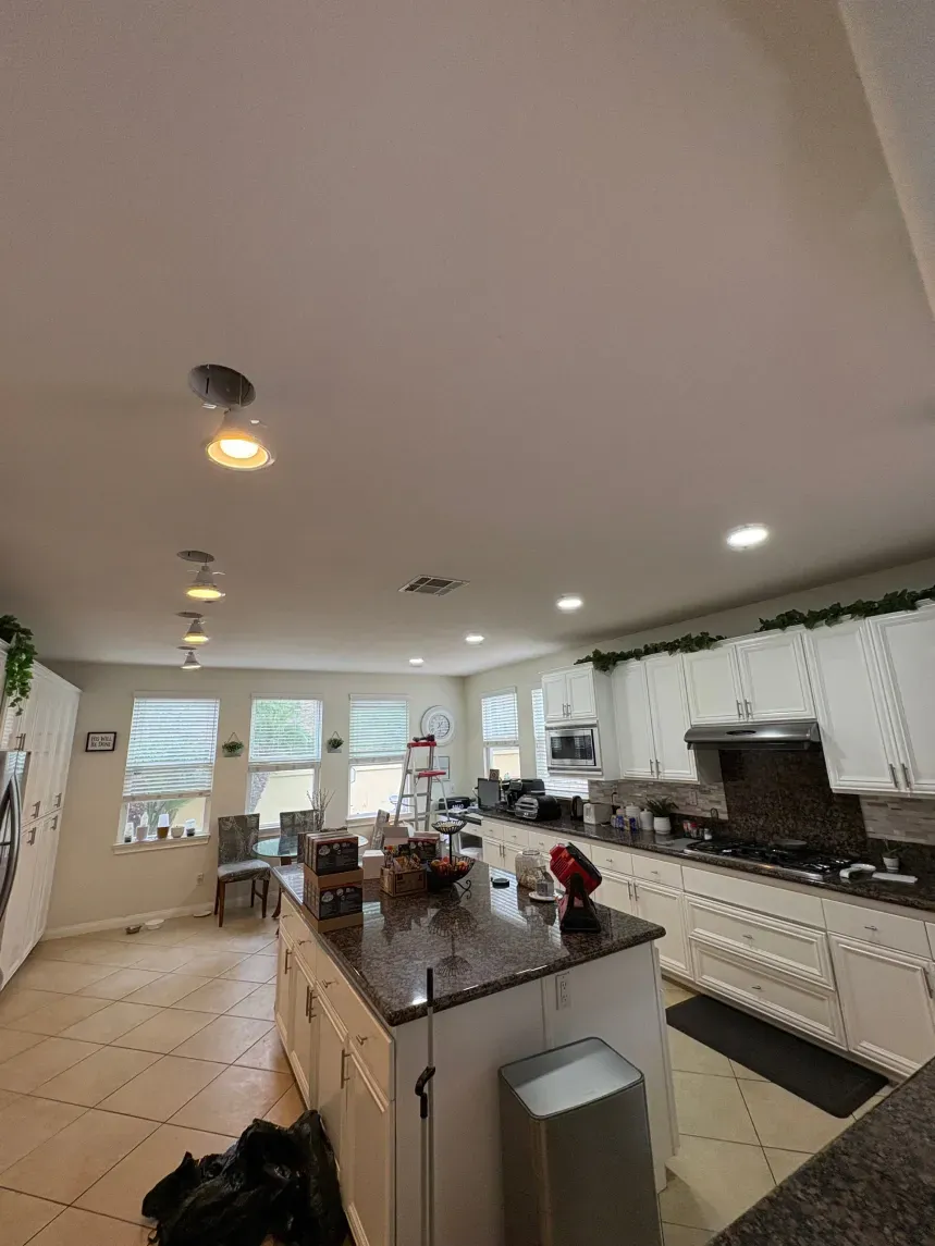 Kitchen interior with white cabinets, island, and recessed lighting. A ladder is present.