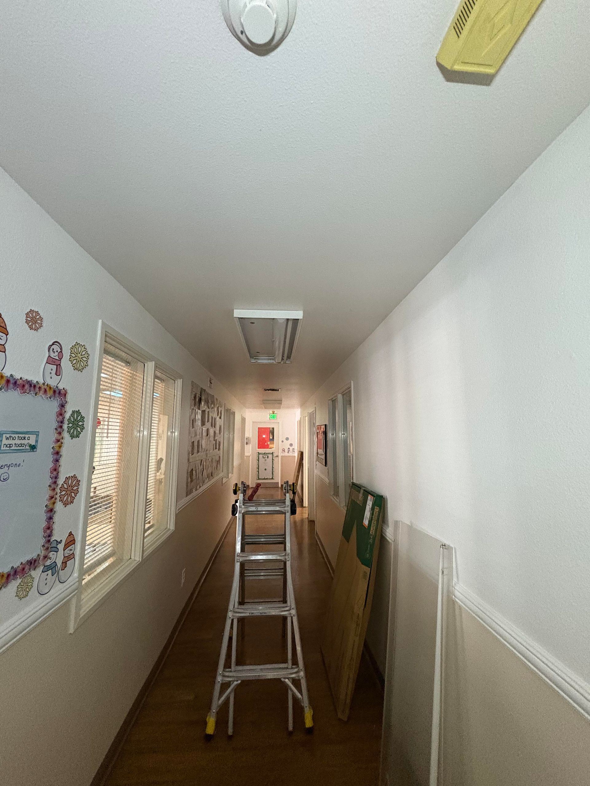 Person on ladders working on ceiling lights in a room with a fireplace and skylight.