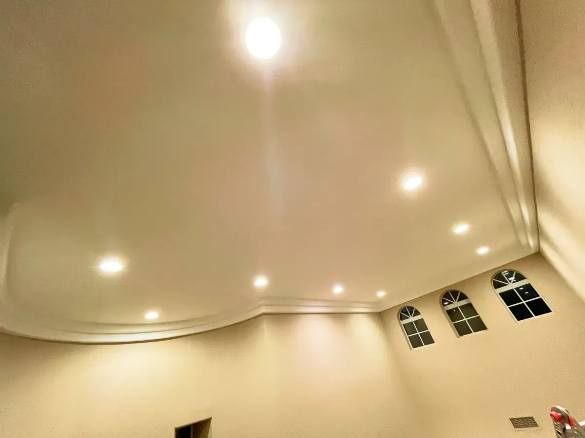 Cream-colored ceiling with recessed lights, curved molding, and arched windows along a beige wall.