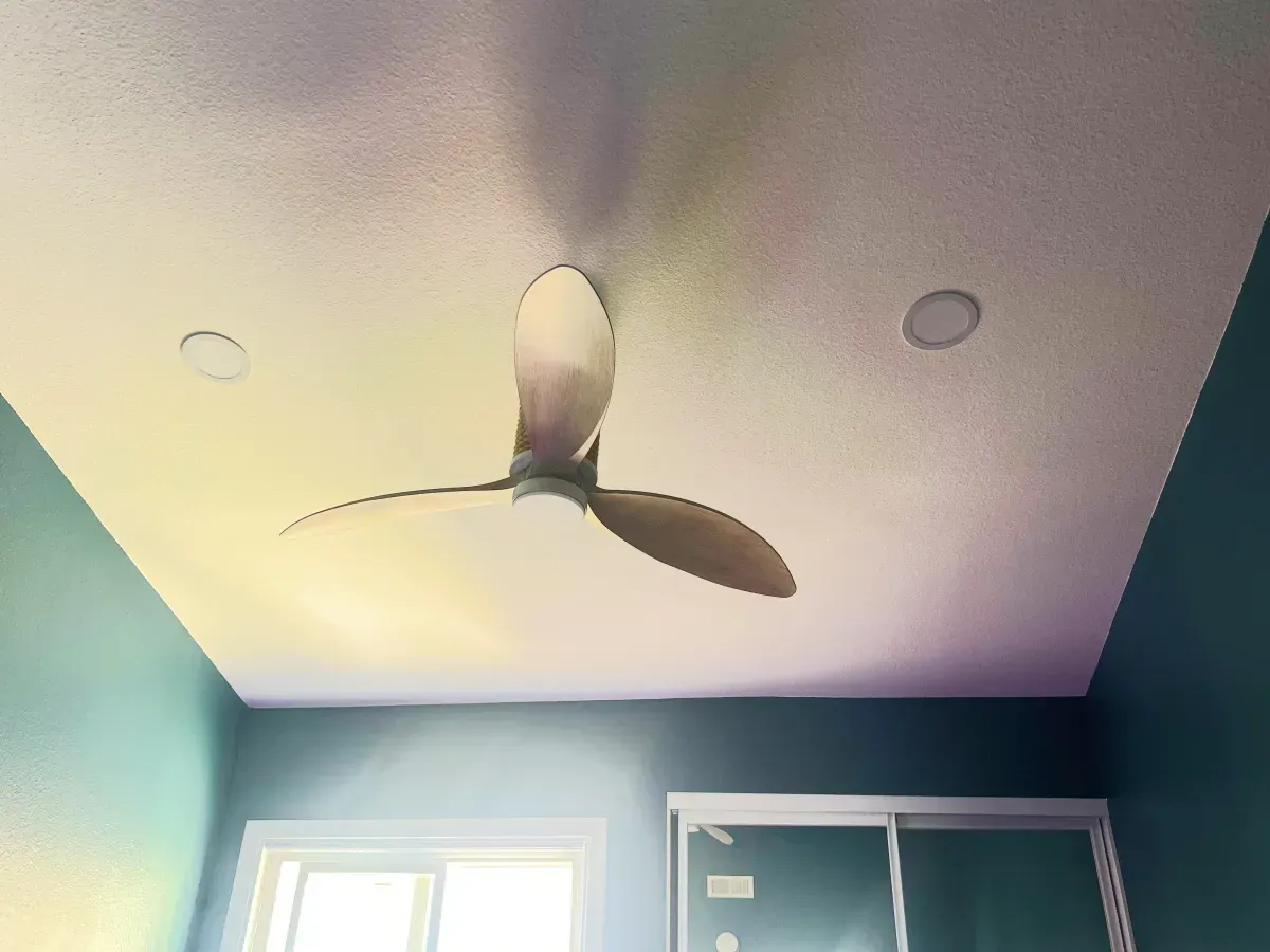 Ceiling fan on a white ceiling with two recessed lights. Blue wall and window visible.