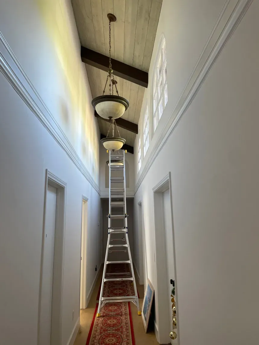Hallway with ladder propped up; two pendant lights suspended from the ceiling.