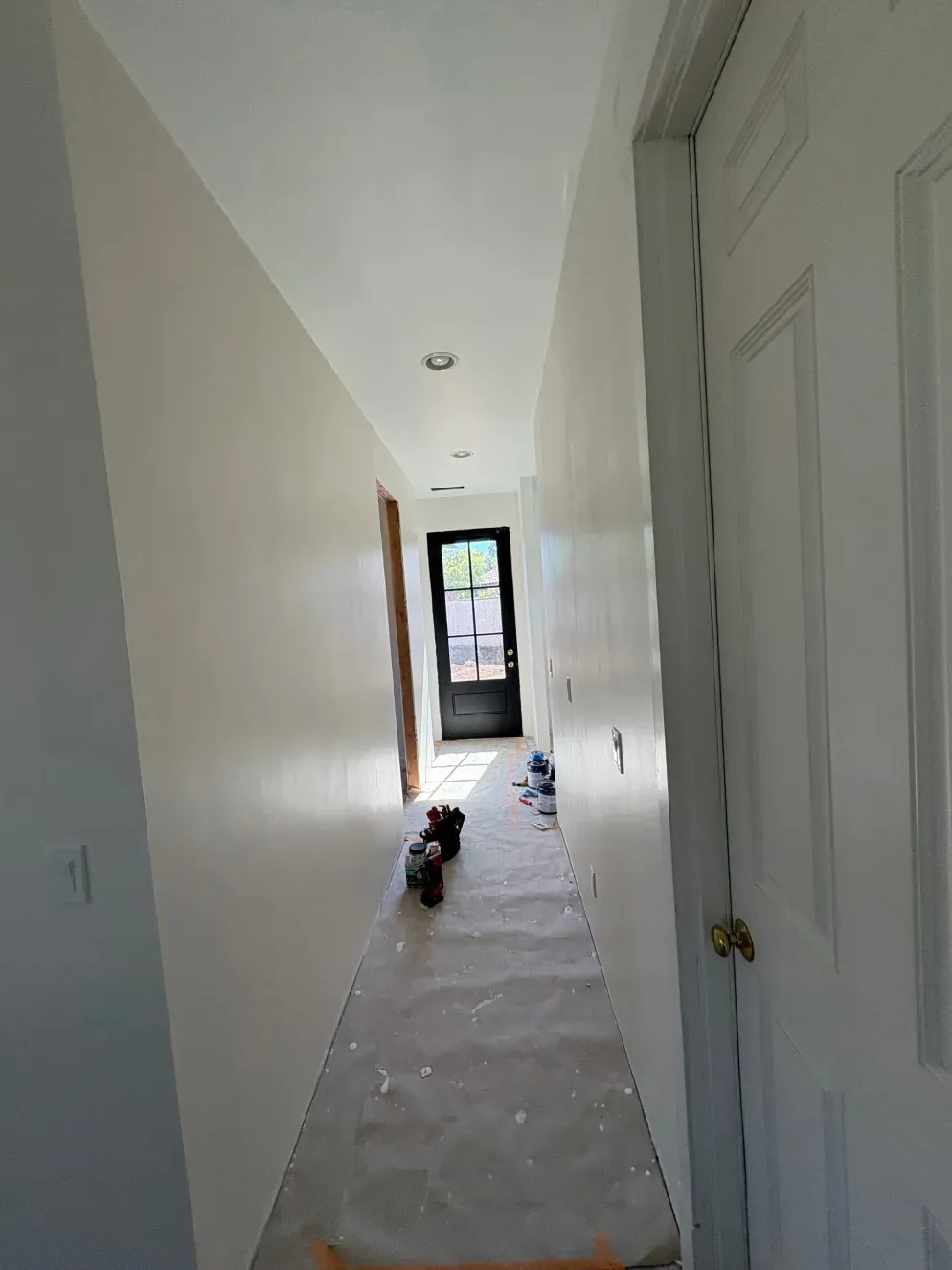 Narrow hallway with off-white walls, a white door on the right, and a door to the outside at the end.