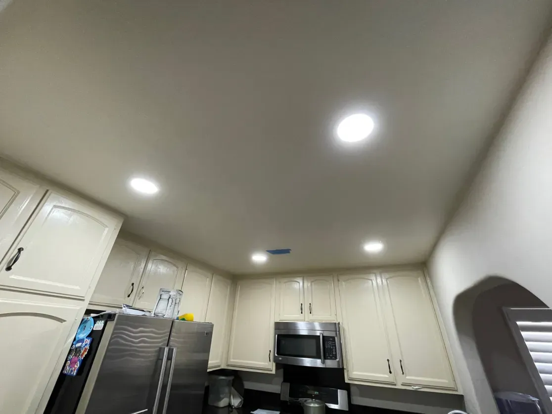 Kitchen ceiling with recessed lights above cream cabinets and stainless steel appliances.