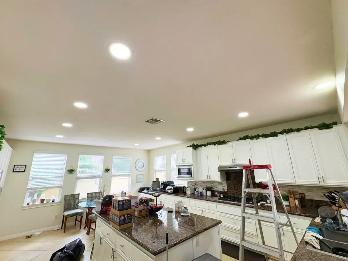 Bright kitchen with an island, cabinets, windows, and recessed lighting. A ladder is set up near the range.