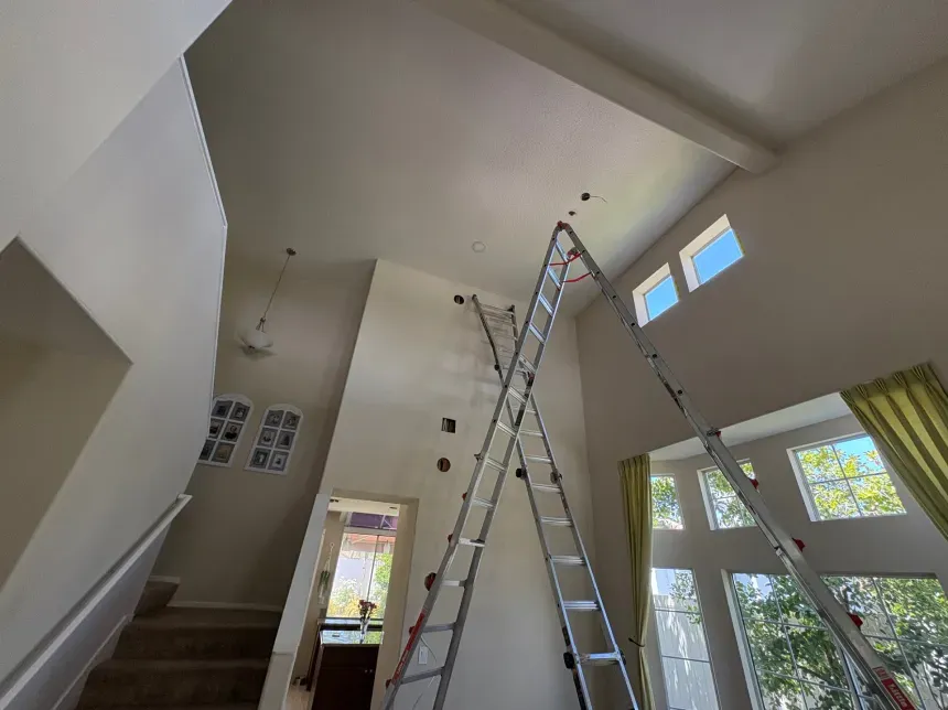 Two ladders crossed inside a house with high ceilings and light-colored walls; undergoing construction.