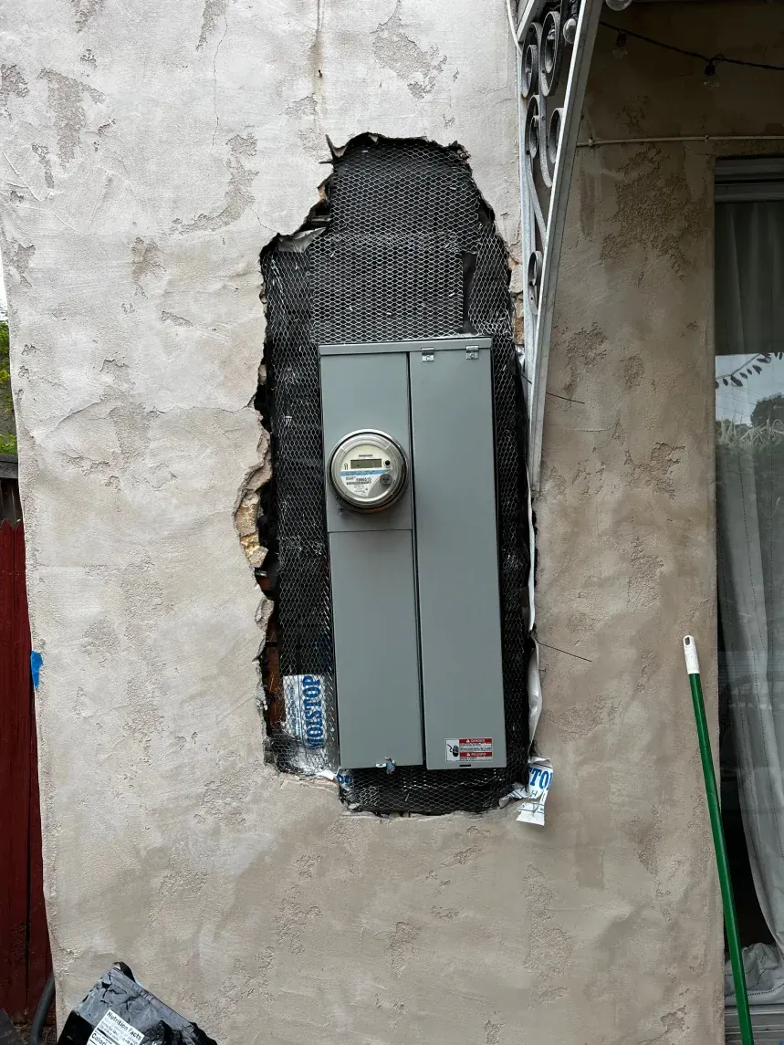 Electrical meter box recessed in a stucco wall, with exposed dark mesh backing.