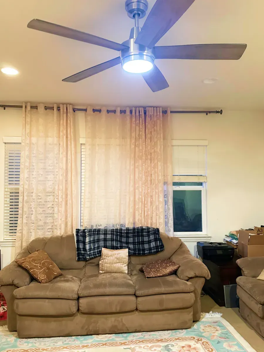 Living room with a brown couch, curtains, and ceiling fan.