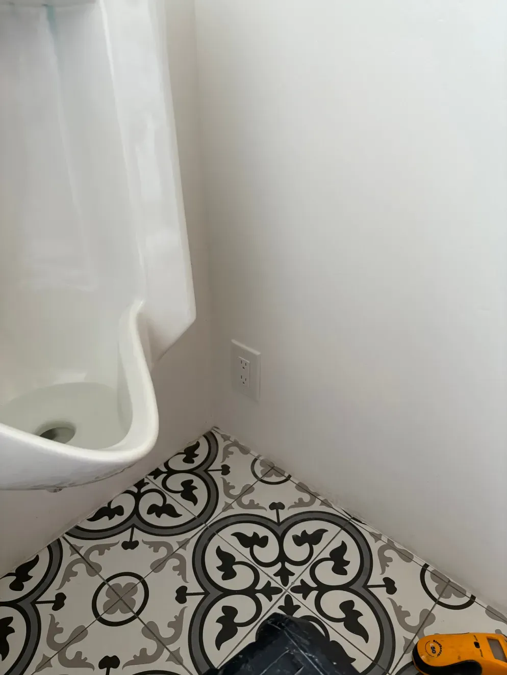 Bathroom corner with patterned floor, white sink, and electrical outlet on the wall.