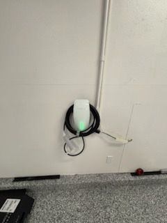 Wall-mounted electrical device with coiled black and white cables against a beige wall.