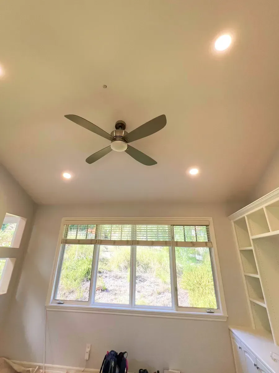 Ceiling with fan and recessed lights above a window with a view and built-in shelves.