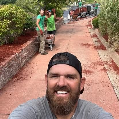 Man taking selfie in front of landscaping crew spreading mulch.
