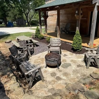Cabin patio with wooden chairs around a fire pit, picnic table nearby.