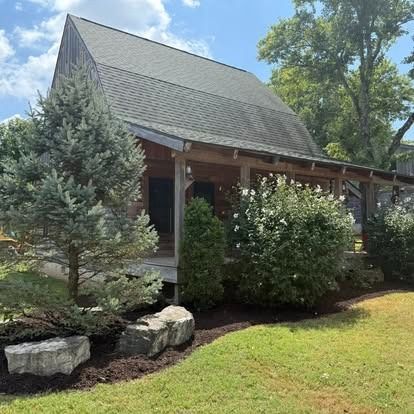 Rustic cabin with wooden porch, landscaping, and green lawn.