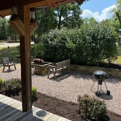 Patio with gravel, fire pit, grill, bench, and shrubs, viewed from a porch with lanterns.