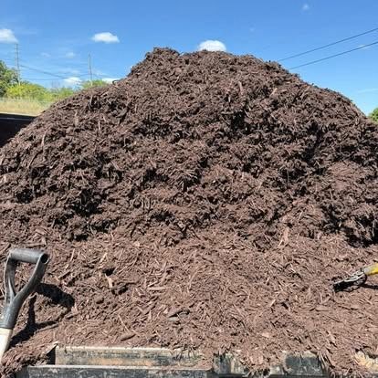 Large pile of dark brown mulch with a shovel on a sunny day.