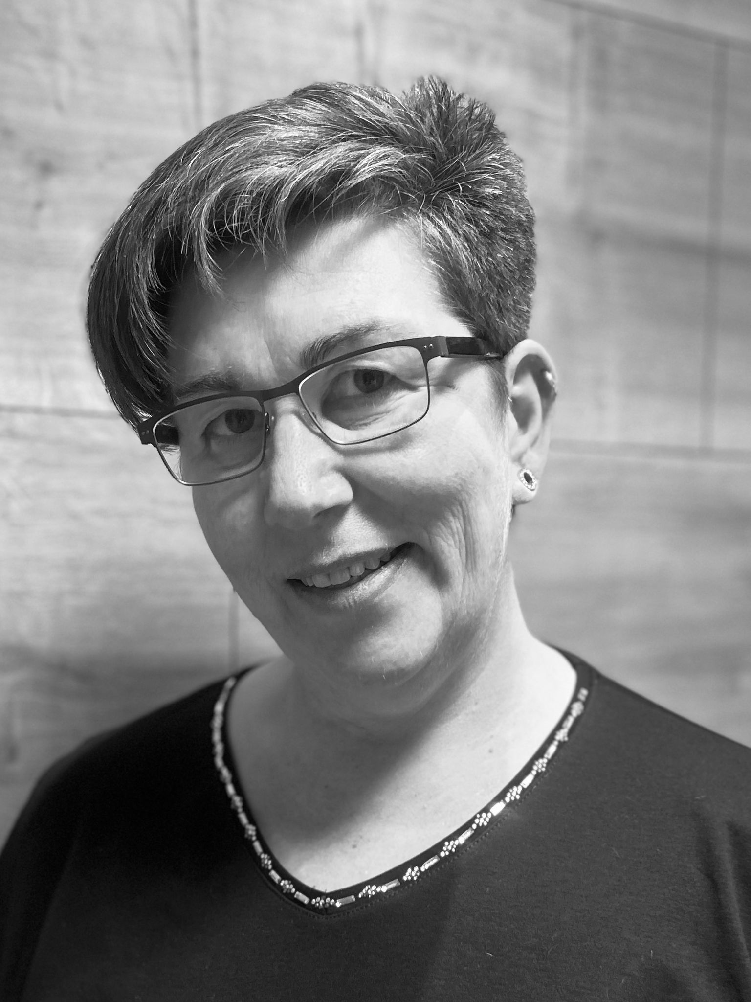 Eine Frau mit Brille und weißem Hemd lächelt auf einem Schwarzweißfoto.
