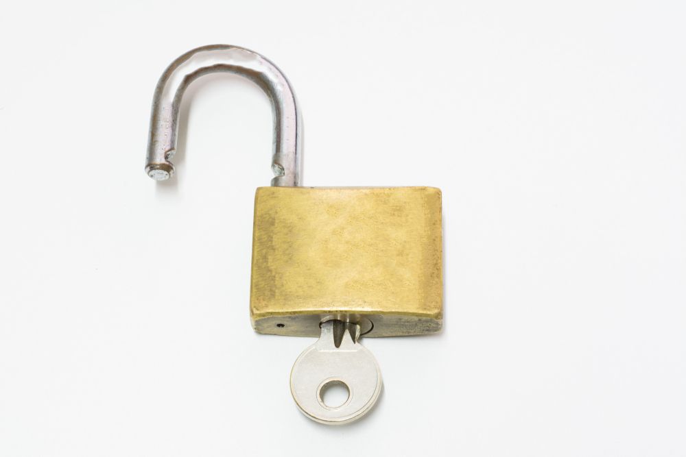 An Open Padlock With A Key Sticking Out Of It On A White Background — Port Macquarie Locksmiths In Wauchope, NSW