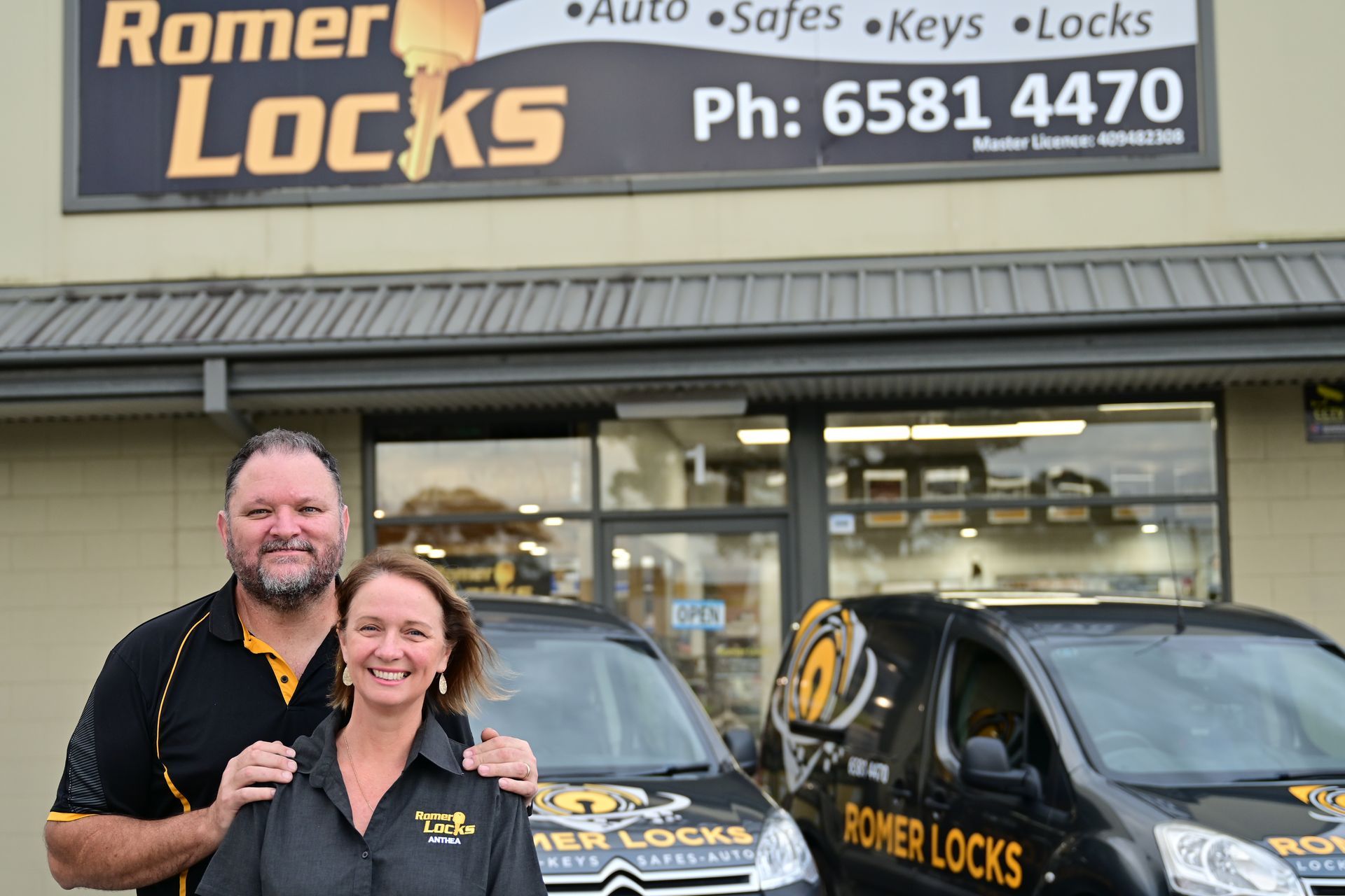 A Man And A Woman Are Standing In Front Of A Store Called Romer Locks — Port Macquarie Locksmiths In Port Macquarie, NSW