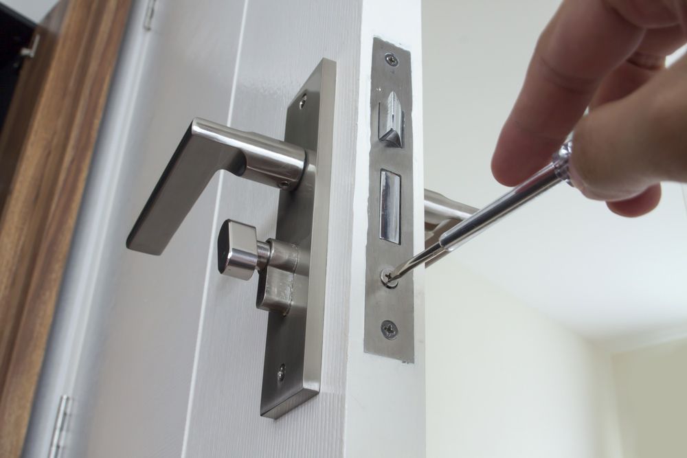 A Person Is Fixing A Door Lock With A Screwdriver — Port Macquarie Locksmiths In Port Macquarie, NSW